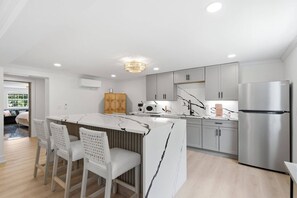 Een moderne keuken met een centraal eiland, roestvrijstalen apparatuur en een eetgedeelte met witte stoelen.