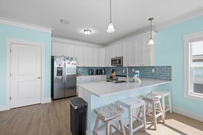 A modern kitchen with white cabinets, stainless steel appliances, a central island with bar stools, and a blue tiled backsplash. - Fort Morgan Beach Escape-Heritage Shores-Dog Friendly-Signature Properties (Gulf Shores)