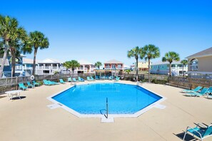 A swimming pool with lounge chairs and palm trees, surrounded by buildings with balconies. - Fort Morgan Beach Escape-Heritage Shores-Dog Friendly-Signature Properties (Gulf Shores)