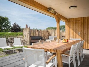 Ein Essbereich im Freien mit einem Holztisch, weißen Stühlen, einem Grill und Blick auf den Garten.