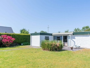 A small, single-story building with a green roof and white exterior walls, surrounded by a well-maintained lawn and flowering bushes. - Holiday Home in Renesse With Swimming Pool (Renesse)
