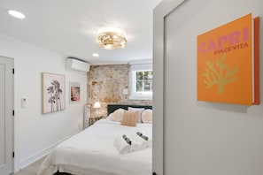 A bedroom with a brick wall, a bed with white bedding, a lamp, and a framed picture on the wall. - Games| Pool | Sleeps 12 | Chef Kitchen (Wilmington)