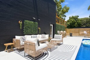 An outdoor patio with wicker furniture, a pool, and a black wall with greenery. - Games| Pool | Sleeps 12 | Chef Kitchen (Wilmington)