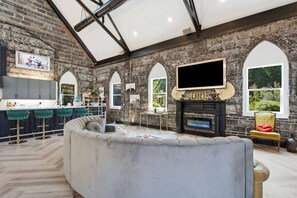 A spacious living area with a fireplace, a television mounted on the wall, and a kitchen area with bar stools. - Games| Pool | Sleeps 12 | Chef Kitchen (Wilmington)