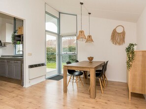 A modern kitchen with a built-in oven, a dining area with a wooden table and chairs, and a large window providing a view of the outdoors. - Holiday Home in Renesse With Swimming Pool (Renesse)