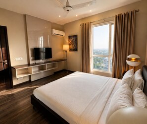 A hotel room with a large bed, a TV, a desk with a lamp, and a window with curtains. - Elysium Serviced Apartment (Islamabad)