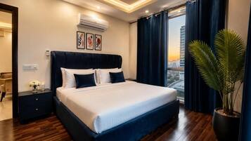 A hotel room with a large bed, a nightstand, a potted plant, and a city view.