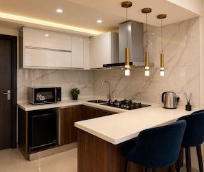 Cocina moderna con microondas integrado, estufa y pileta, destacando un protector contra salpicaduras de mármol e iluminación colgante.