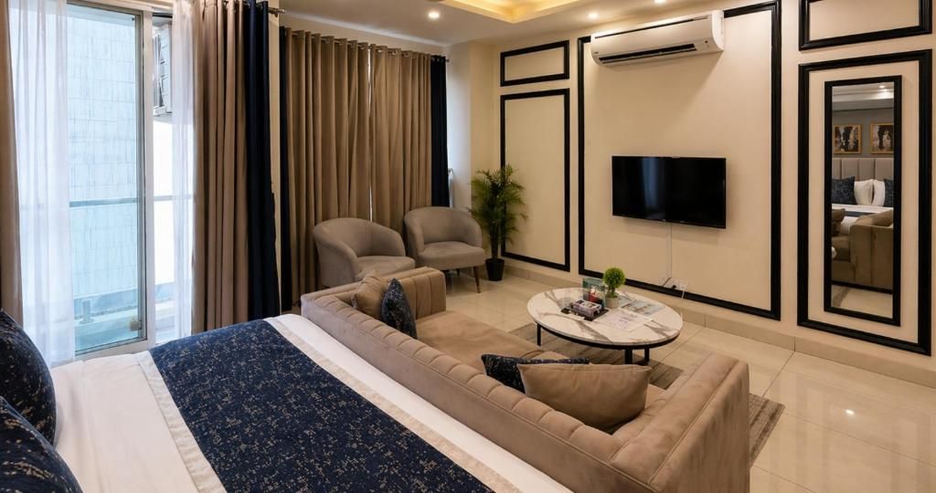 Una habitación de hotel moderna con una cama grande, dos sillones, un sofá, una mesa de centro y un televisor de pantalla plana montado en la pared.