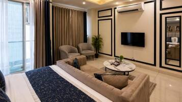 Una habitación de hotel moderna con una cama grande, dos sillones, un sofá, una mesa de centro y un televisor de pantalla plana montado en la pared.