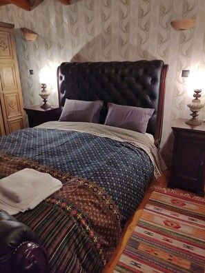 A bedroom with a large bed, a wooden wardrobe, and a patterned rug.