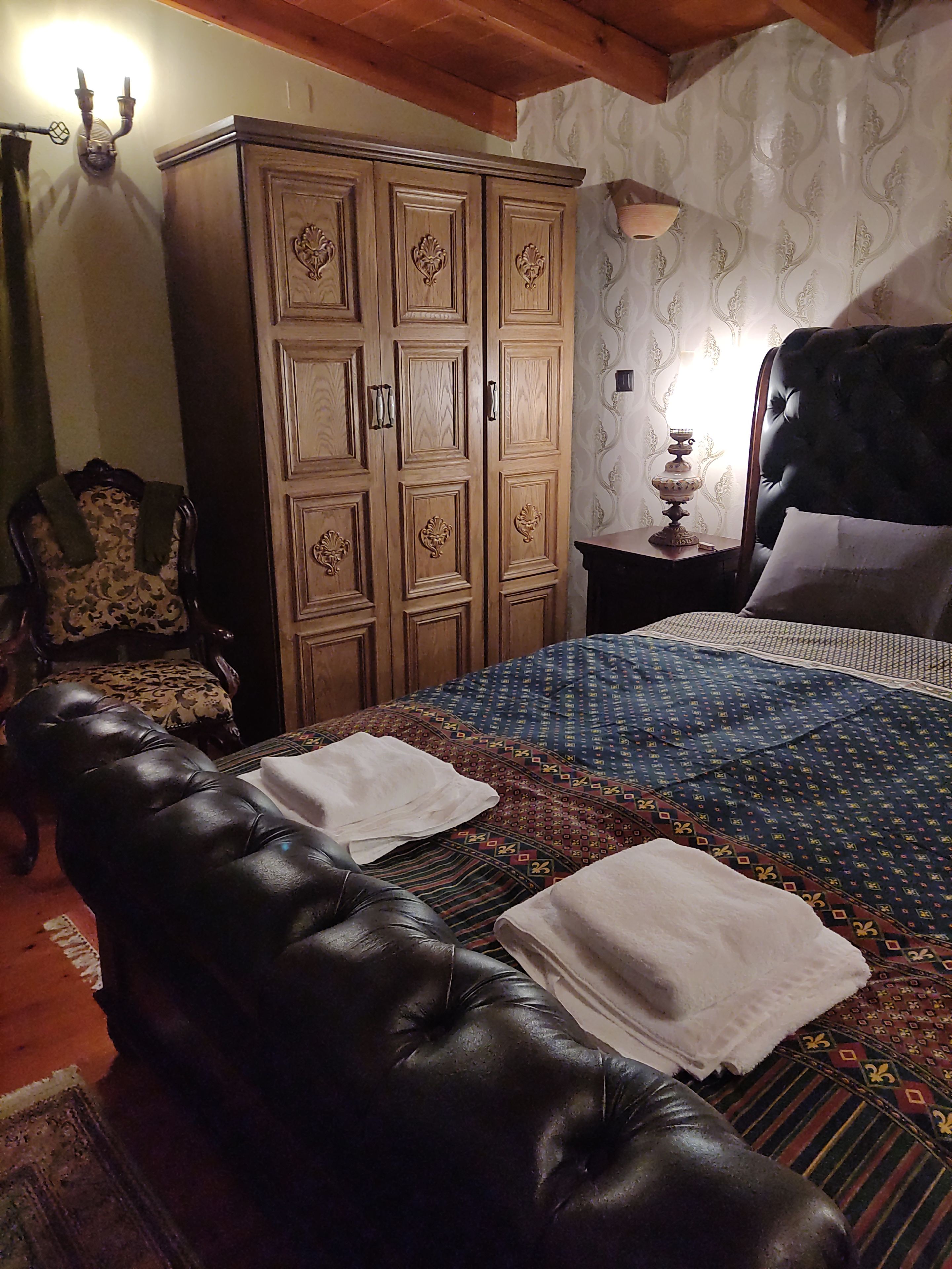 Een slaapkamer met een groot bed, een leren bank, een houten garderobe en een behang met een patroon.