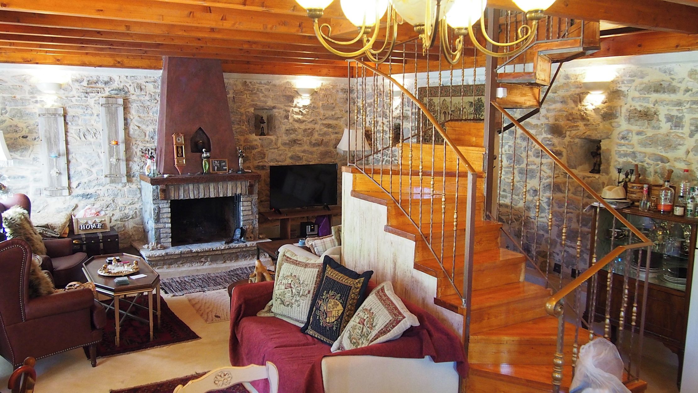 A cozy living room with a stone fireplace, wooden staircase, and a television.