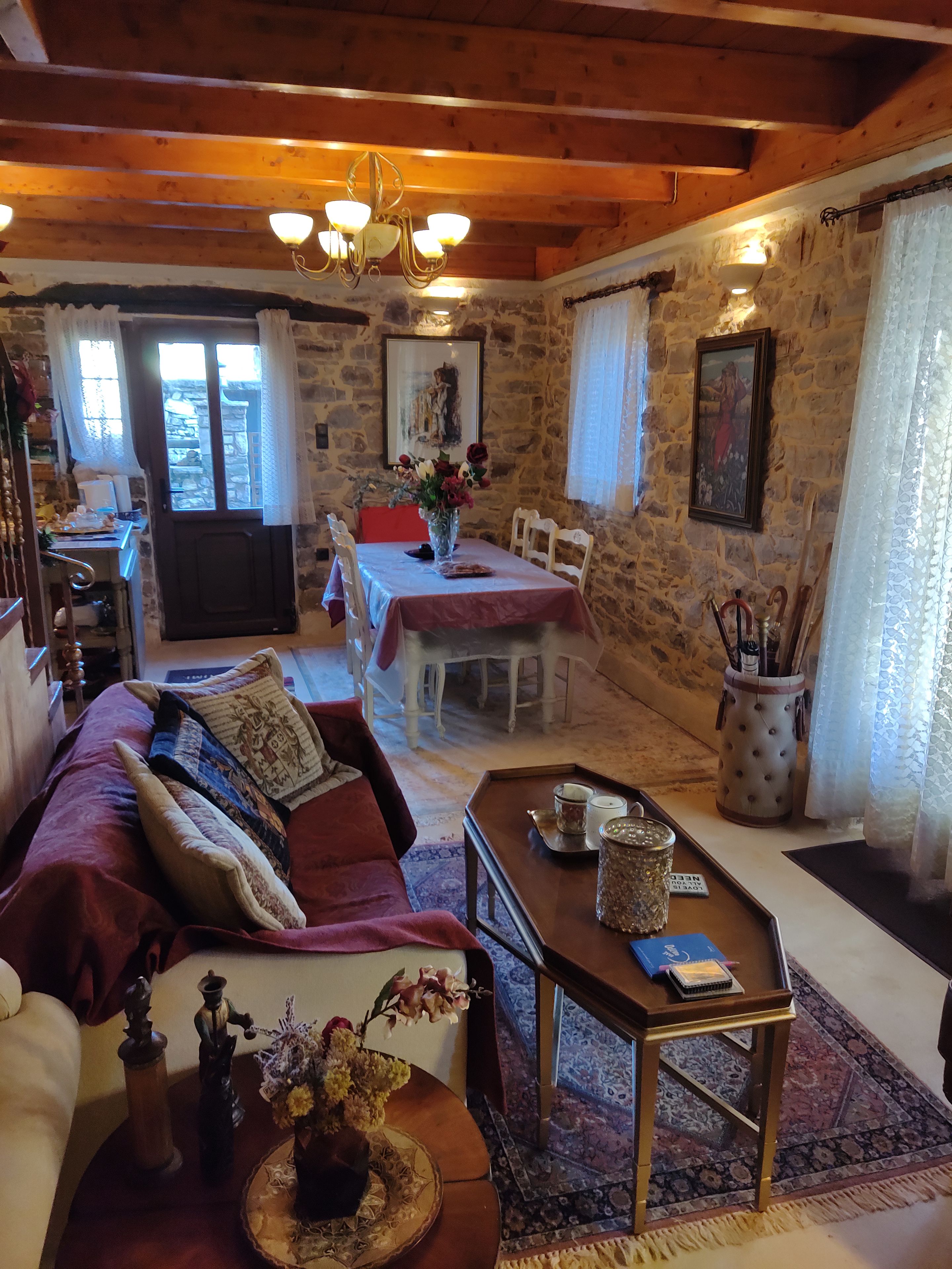 A cozy room with a wooden ceiling, a dining area with a table and chairs, and a sofa with cushions.