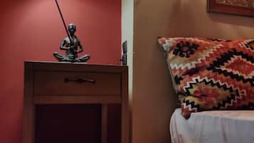 A room with a bed, a nightstand with a lamp, a wall-mounted light fixture, and a patterned rug.