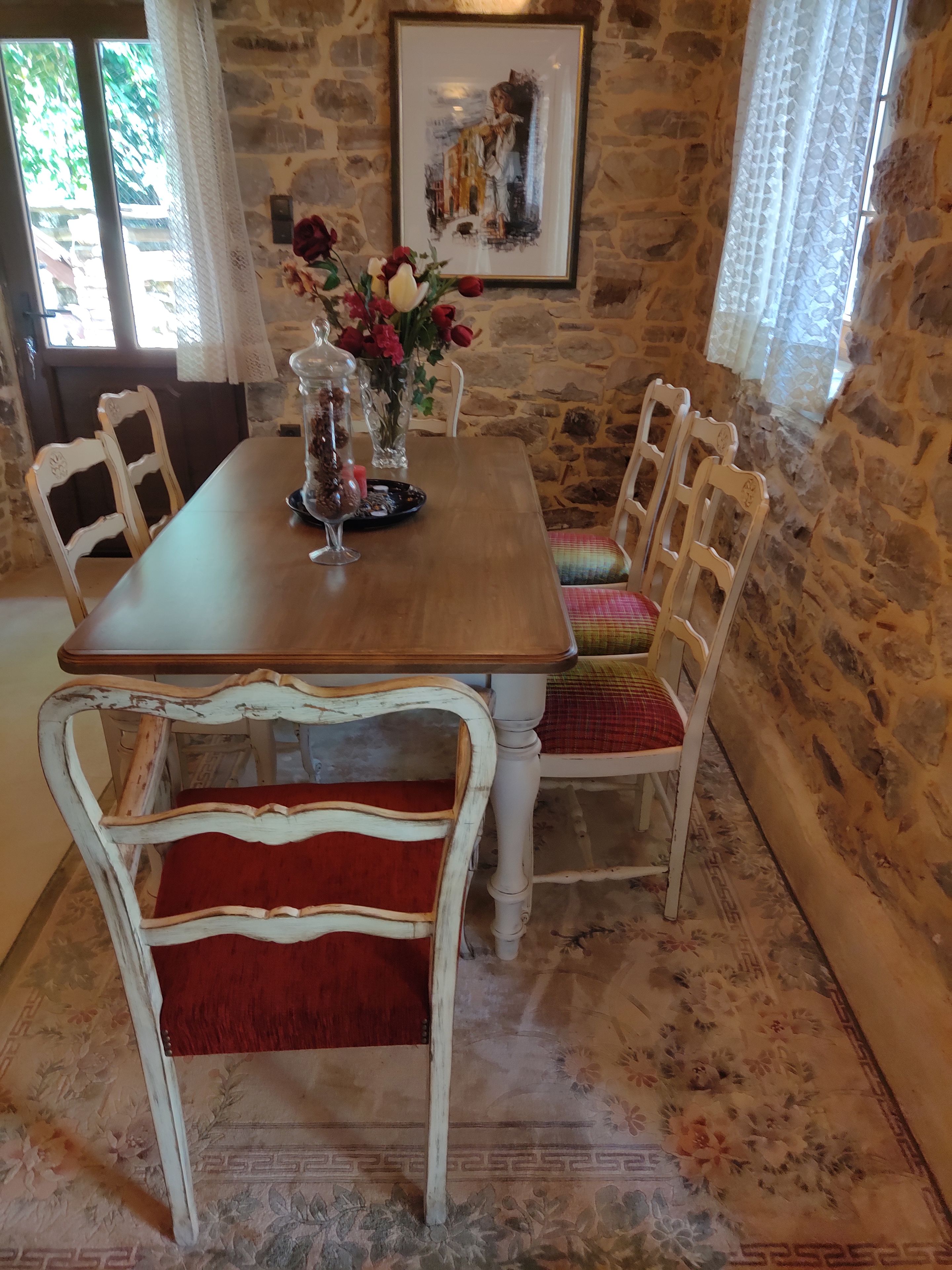 A stone-walled room with a wooden dining table, white chairs, and a floral arrangement.