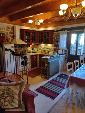 A cozy kitchen with wooden beams, stone walls, and a dining area with a table and chairs.