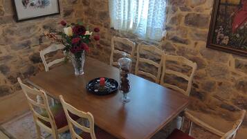 Un comedor con pared de piedra, una araña y una mesa lista para cuatro comensales.