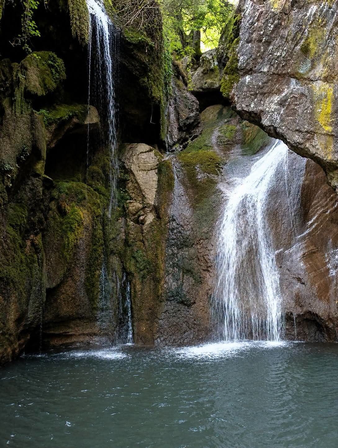 A waterfall cascading over moss-covered rocks into a pool of water.