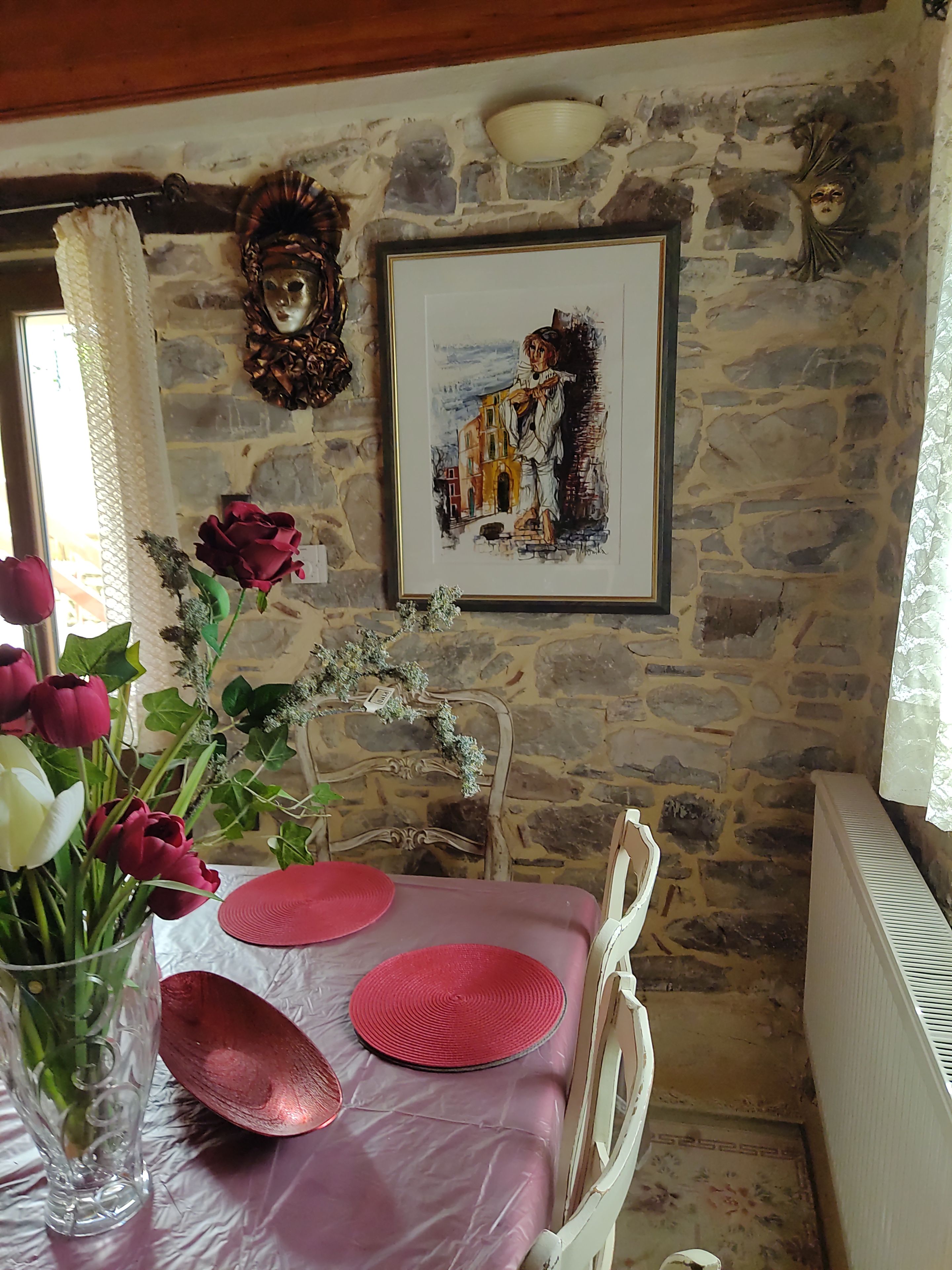Ein Essbereich mit einer Steinwand, einem gerahmten Gemälde, einer Blumenvase und einem Tisch, der mit rosa Unterlagen gedeckt ist.