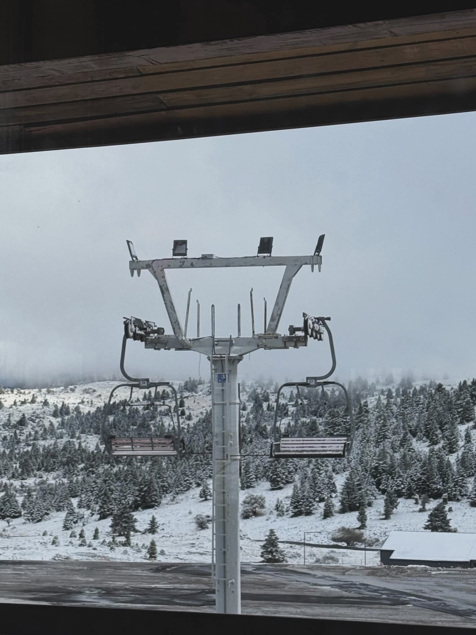 A ski lift chair with a metal frame and two seats, set against a snowy mountain backdrop.