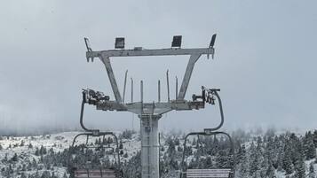 A ski lift chair with a metal frame and two seats, set against a snowy mountain backdrop.