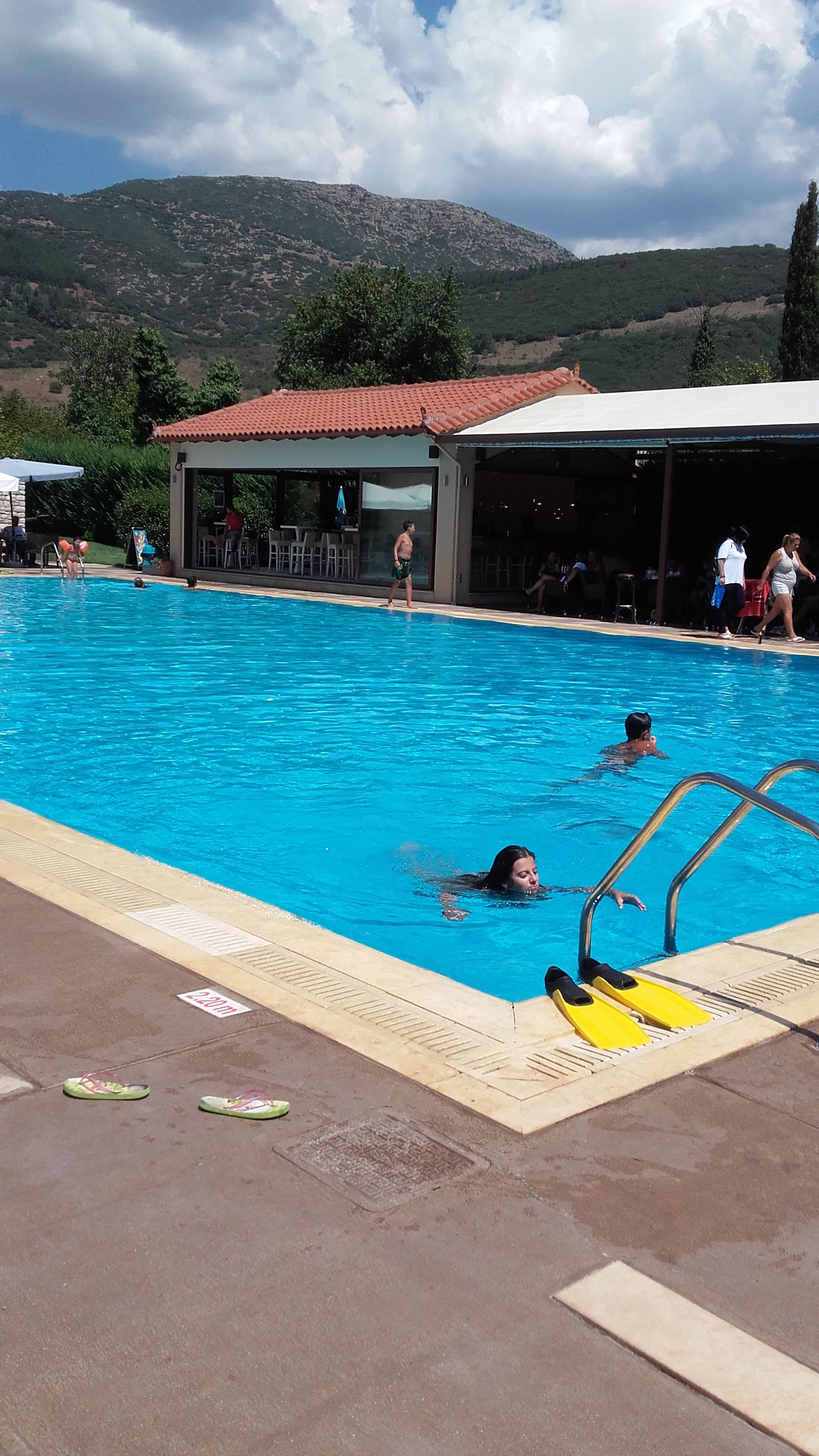 Una piscina con agua cristalina azul, rodeada por una zona cubierta con techo de baldosas.