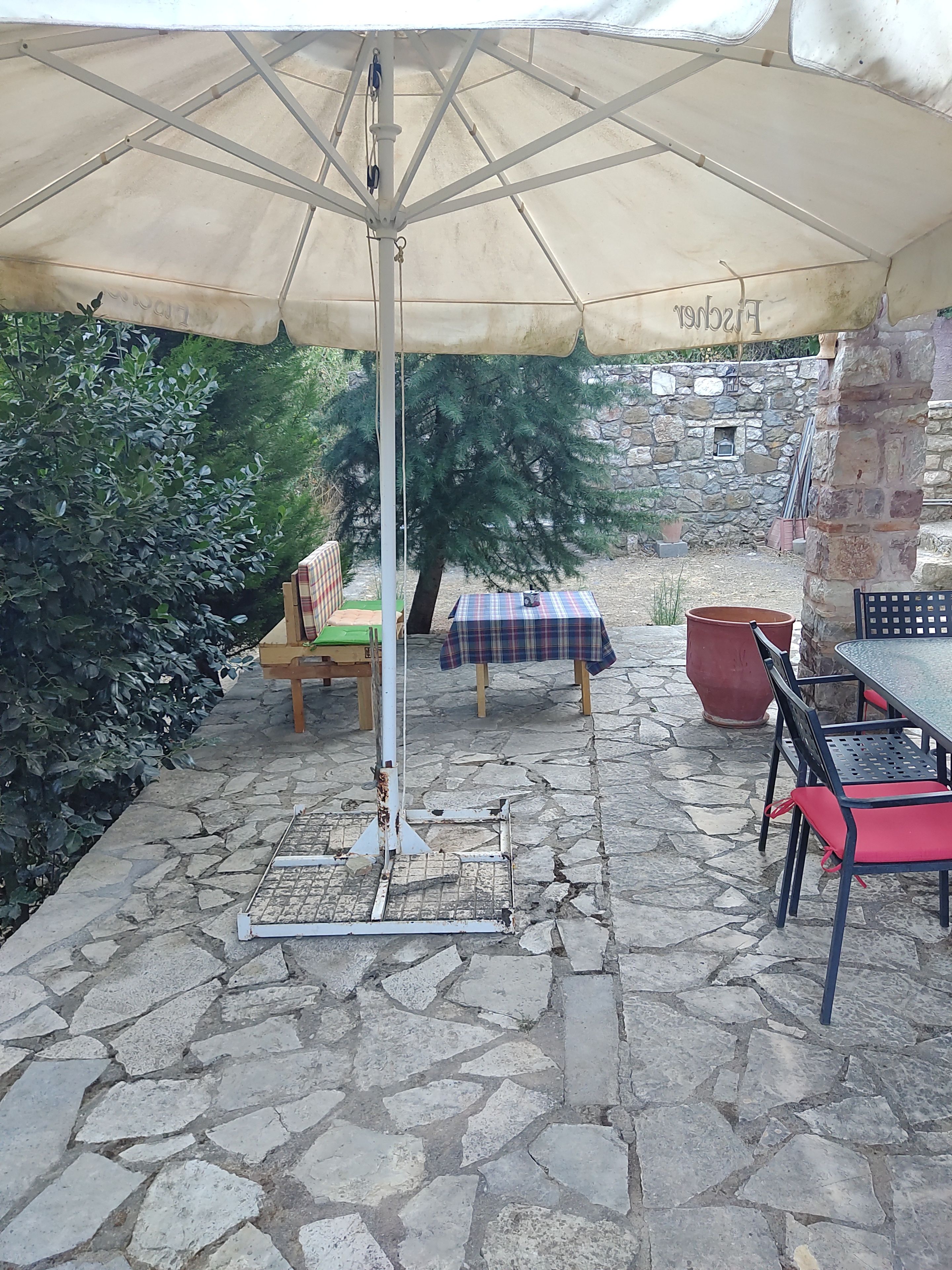 An outdoor patio with a table and chairs, a large umbrella, and a stone wall in the background.