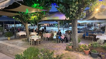Un área de comedor al aire libre con mesas y sillas, rodeada de follaje y árboles.