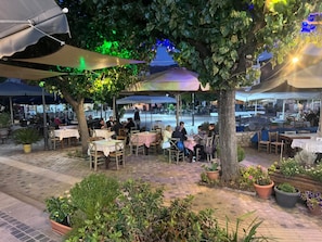 Un espace de restauration en plein air, avec des tables et des chaises, entouré de verdure et d’arbres.
