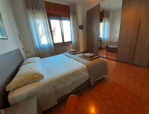 Ein Hotelzimmer mit Bett, Nachttisch, Fenster mit Vorhängen und Blick auf ein weiteres Zimmer.
