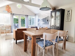 A dining area with a wooden table and chairs, a cabinet, and a view of the outdoors through large windows. - Ok45 Holiday Home Oostkapelle (Oostkapelle)