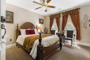 A bedroom with a large bed, a ceiling fan, a window with curtains, and a chair.