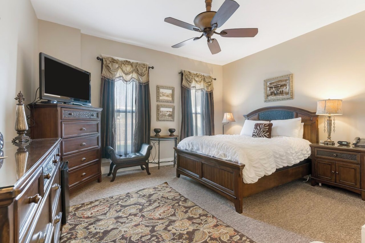 A bedroom with a bed, dresser, television, and a ceiling fan.