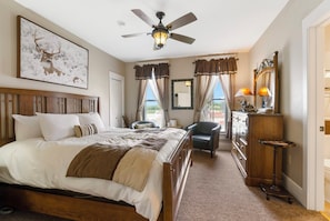 A hotel room with a large bed, a ceiling fan, a desk with a lamp, and a view of the outdoors. - The Branson Hotel (Branson)