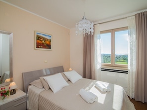 A hotel room with a bed, a bedside table with a lamp, a painting on the wall, and a window with curtains. - Villa in Fazana With Swimming Pool (Fazana)