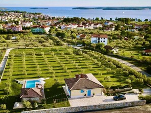 A residential area with a swimming pool, a house with a blue door, and a view of the sea. - Villa in Fazana With Swimming Pool (Fazana)