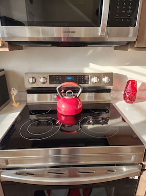 A stainless steel Samsung microwave above a stove with a red kettle on it.