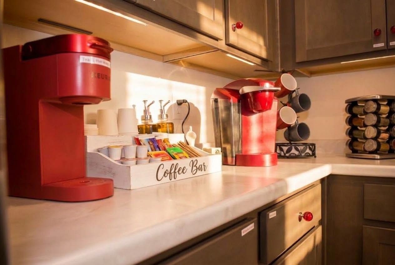 A kitchen with a coffee bar, including a coffee machine, cups, and a container with coffee pods.