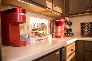 A kitchen with a coffee bar, including a coffee machine, cups, and a container with coffee pods.