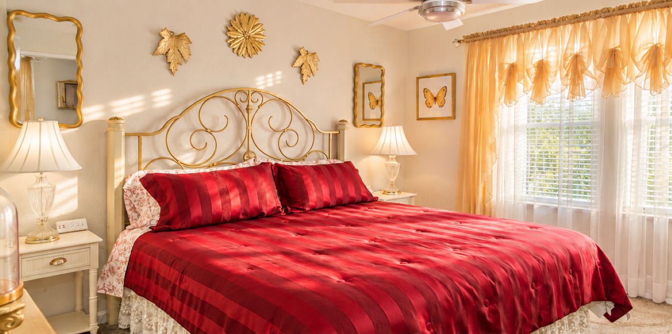 A bed with a red bedspread and gold headboard, two bedside lamps, and decorative wall art.