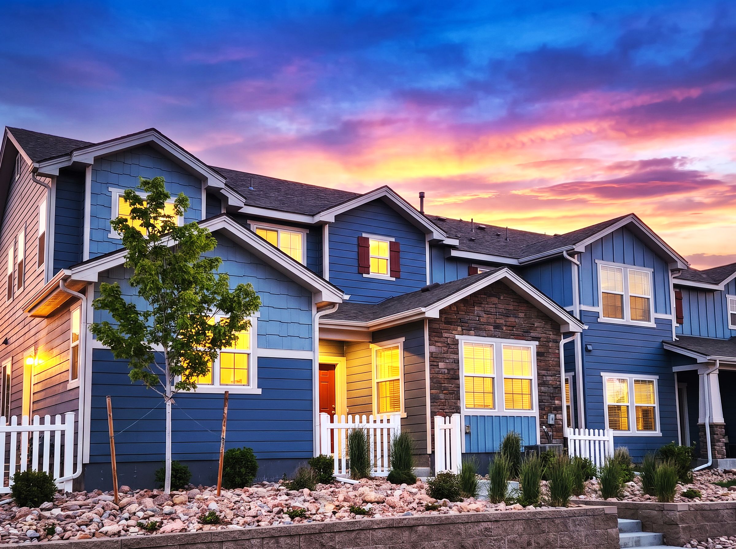 A row of blue houses with white railings and a sunset sky.