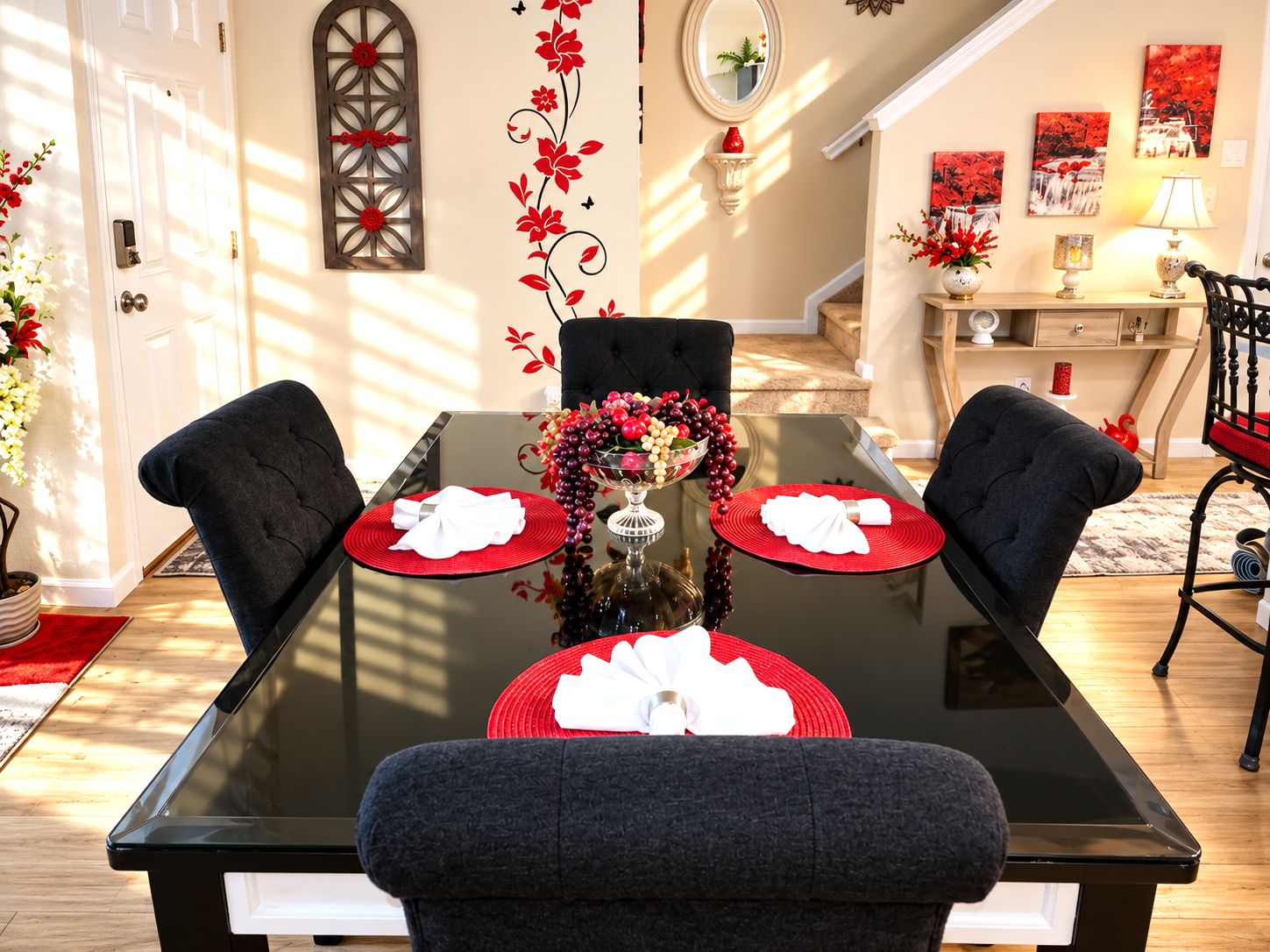 A dining area with a glass table, two black upholstered chairs, and a vase with red flowers.