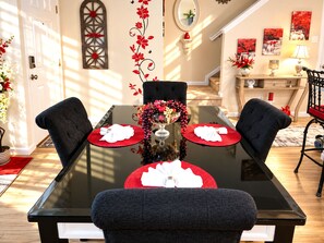 A dining area with a glass table, two black upholstered chairs, and a vase with red flowers.