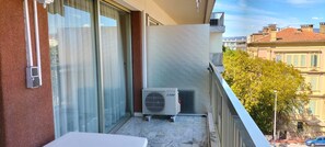 Ein Balkon mit einer Schiebetür, einer weißen Klimaanlage und Blick auf Gebäude und Bäume.