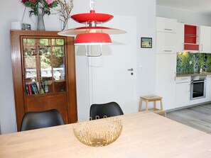 A dining area with a wooden table, chairs, a red pendant light, and a bookshelf with books. - To the W9 Lighthouse Prerow (Ostseebad Prerow)