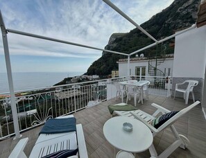 Ein Balkon mit Blick auf das Meer, ein Tisch, Stühle und ein kleiner Tisch mit einer Tasse.