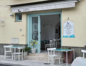 Ein Restaurant namens Zaghéra mit Außenbereich und einer Schautafel, die die angebotenen Speisen auflistet.