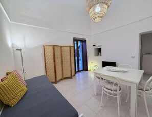 Ein Zimmer mit einem Bett, einem Esstisch mit Stühlen, einem Kleiderschrank und einer Deckenleuchte.