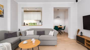 Una sala moderna con un sofá seccional gris, una mesa de centro de madera y un comedor con una mesa redonda y sillas verdes.